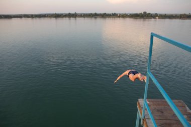 gün batımında göl suyunda kuleden atlayan adam