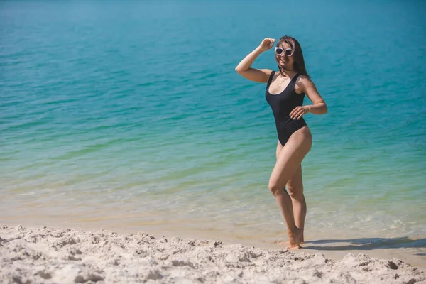 Lächelnde Frau mit Sonnenbrille und schwarzem Badeanzug im blauen klaren Wasser — Stockfoto