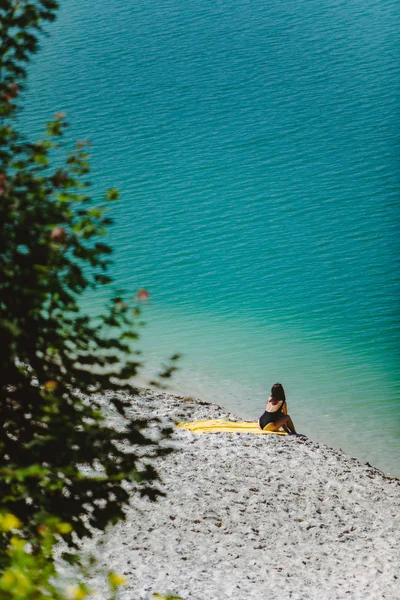 Frau sitzt am Sandstrand und blickt auf blaues, azurblaues Wasser — Stockfoto