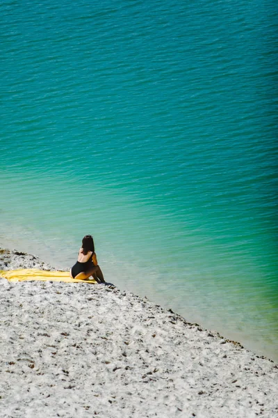 Mulher sentada na praia de areia olhando para a água azul azure — Fotografia de Stock