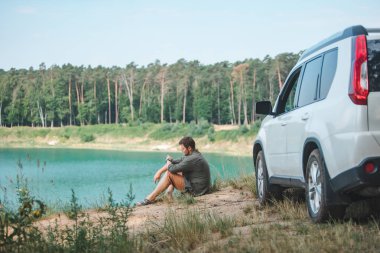 mavi su ile göle bakarak kenarında beyaz SUV araba yakın oturan adam