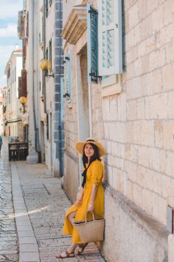 yazlık tatil şehirde taş bina yakınında duran şapka ile yaz sarı elbiseli kadın