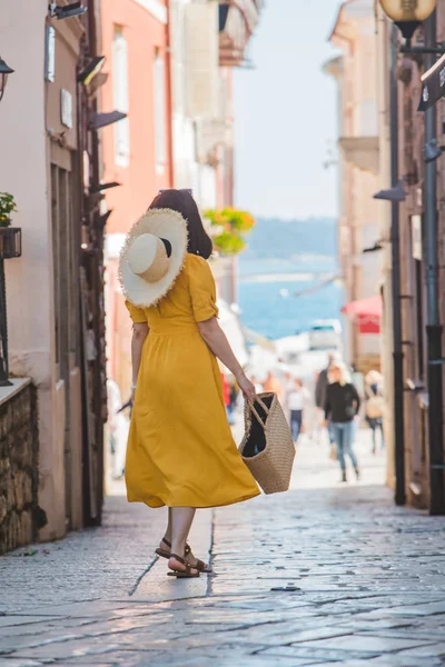 Mladá krásná žena ve žlutých šatech, po malých uličkách v ulicích města na pozadí — Stock fotografie