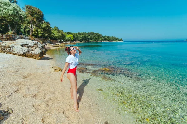 Sexy vrouw in rood badpak en wit t-shirt op zee strand — Stockfoto