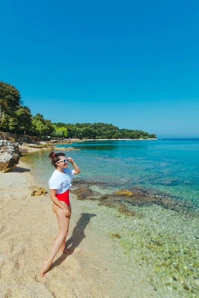Sexy mujer en traje de baño rojo y camiseta blanca en la playa de mar —  Fotos de Stock