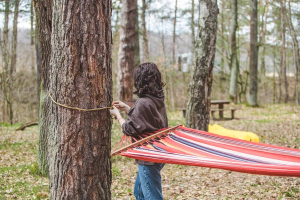 woman ties up hammock in forest