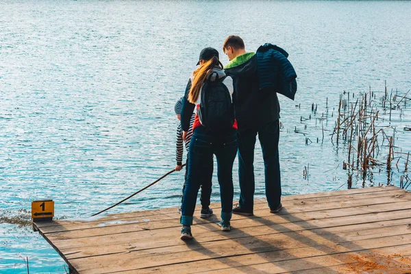 Far och mor med pojke Kid leker med bänken nära vatten — Stockfoto