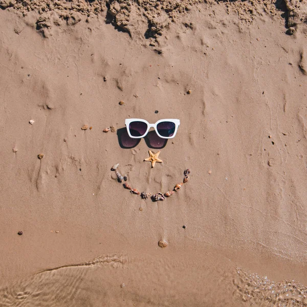 貝殻とサングラスで砂の上に描かれた笑顔の顔 — ストック写真