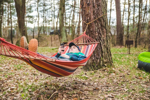 Young man laying in hammock surfing in phone — Stock Photo, Image