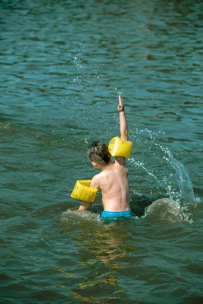 Toddler kid swimming in sea water outdoors with inflatable arms aids on his hands — Stock Photo, Image