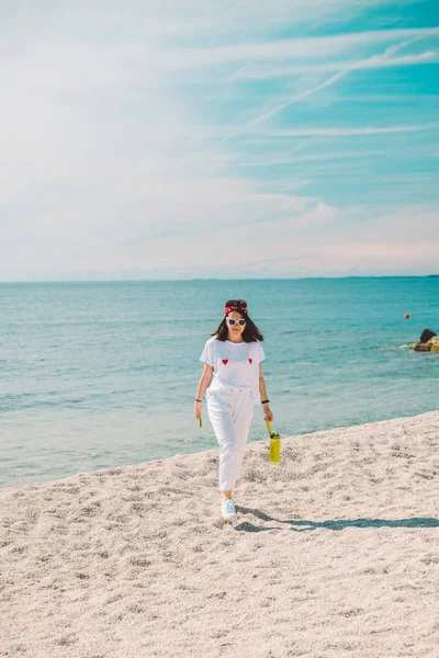 Mulher em roupas brancas andando pela praia do mar em dia ensolarado — Fotografia de Stock