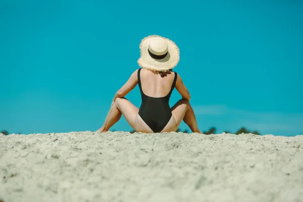 Kilátás hátulról nő a fekete fürdőruhát ül Sand Beach — Stock Fotó