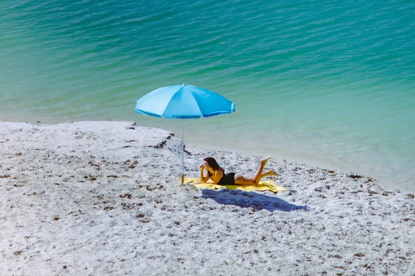 Woman in swimsuit walking by sand beach blue sun umbrella and yellow blanket — Stock Photo, Image