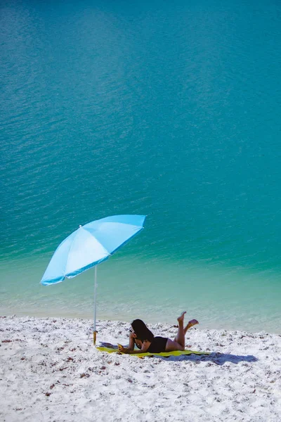 Mulher de maiô andando pela praia de areia guarda-sol azul e cobertor amarelo — Fotografia de Stock