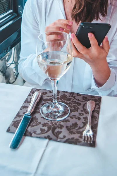 Женщина с бокалом вина сидит в ресторане и смотрит в телефон — стоковое фото