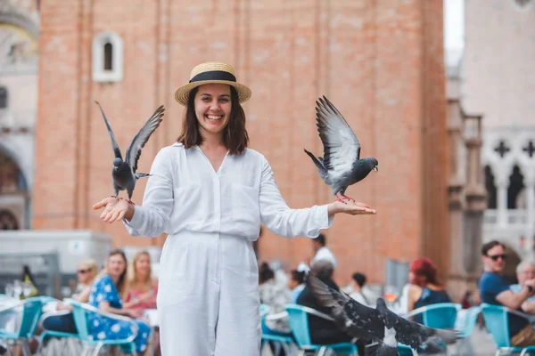 Frau in weißen Kleidern mit Strohhut amüsiert sich mit Tauben auf dem venezianischen Stadtplatz — Stockfoto