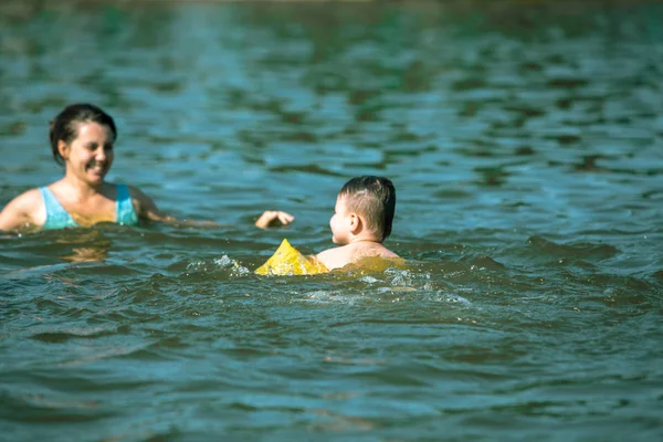 Kleines Kleinkind mit aufblasbaren Armbinden hilft beim Spielen im Wasser mit Mutter im Seewasser — Stockfoto
