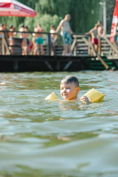 little toddler kid swimming in lake with inflatable arms aids support