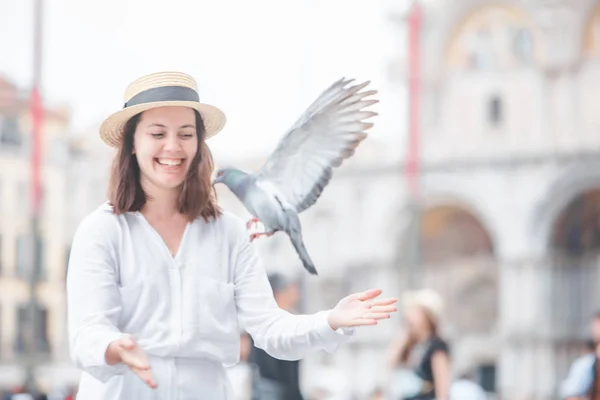 Mujer en ropa blanca con sombrero de paja divirtiéndose con palomas en la plaza de Venecia —  Fotos de Stock