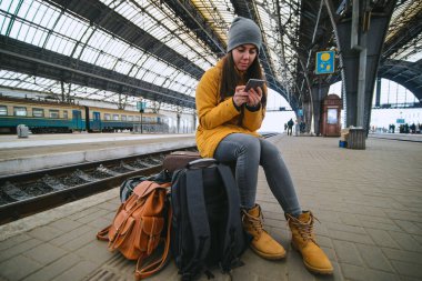 genç kadın çantalarında tren istasyonunda oturup. Treni bekliyorum. kopyalama alanı