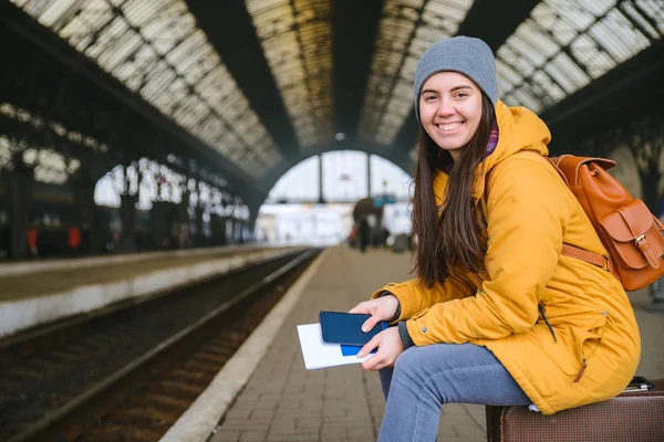 young pretty woman waiting for train at railway station. sit on bags while waiting for train