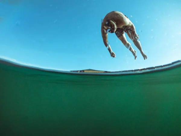 Man jumping from wooden pier in lake water — Stock Photo, Image