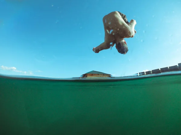 Мужчина прыгает с деревянного пирса в озерной воде — стоковое фото