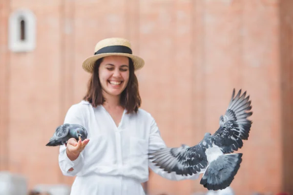 Wanita berpakaian putih dengan topi jerami bersenang-senang dengan merpati di venice city square — Stok Foto