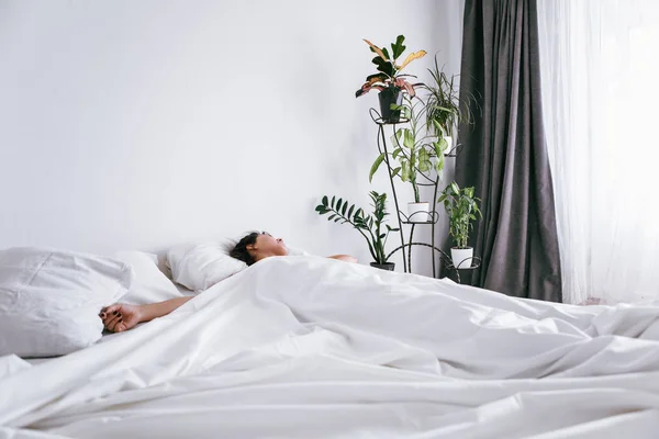Mulher escorregando na cama com lençóis brancos luz solar na janela — Fotografia de Stock
