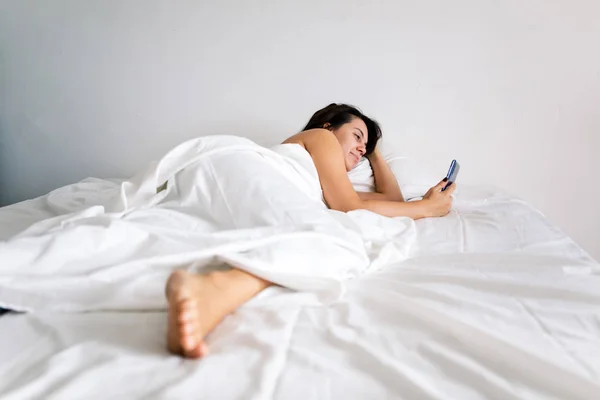 Woman with smartphone in bed with white sheets — Stock Photo, Image