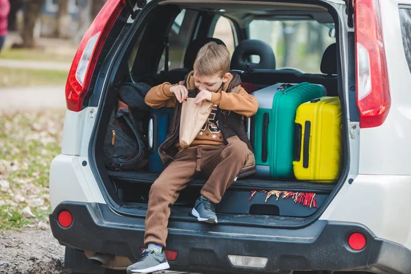 Little kid looking into paper bag with candies sitting in car trunk — Stock Photo, Image