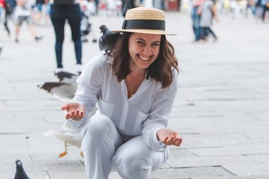 Beyaz giysili, hasır şapkalı kadın Venedik Meydanı 'nda güvercinlerle eğleniyor.