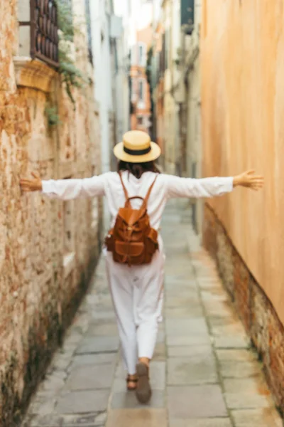 Kvinna i vita kläder i halm hatt och brunt läder ryggsäck Walking by City Street — Stockfoto