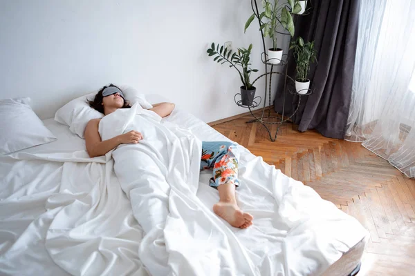 Mulher dormindo em máscara de sono na cama com lençóis brancos — Fotografia de Stock