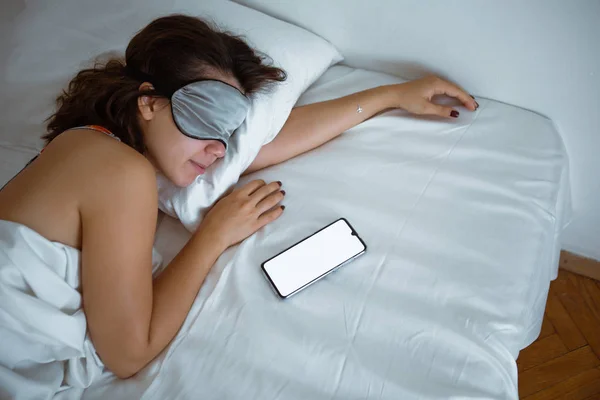 woman sleeping in sleep mask smartphone near her