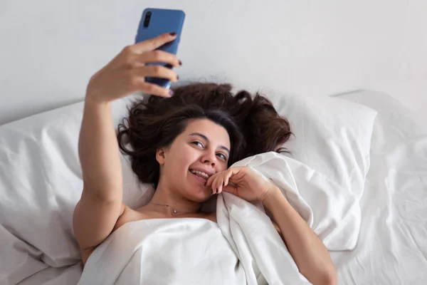 Woman laying in bed taking selfie on the phone — Stock Photo, Image