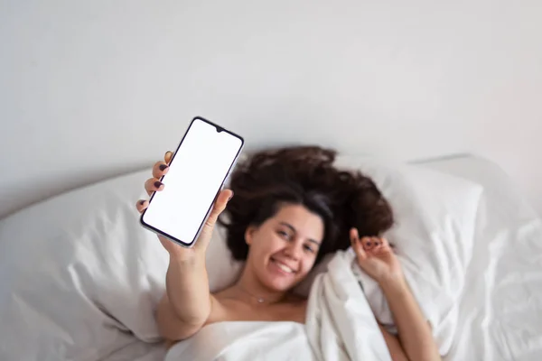 Woman laying in bed showing phone with white screen — Stock Photo, Image