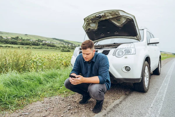 adam telefon ile kırık arabanın yanında oturan, yardım arıyor