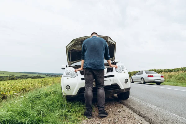 Hombre mirando el motor en el coche roto en la carretera —  Fotos de Stock