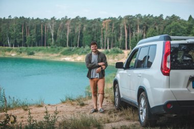 mavi su ile göle bakarak kenarında beyaz SUV araba yakın adam