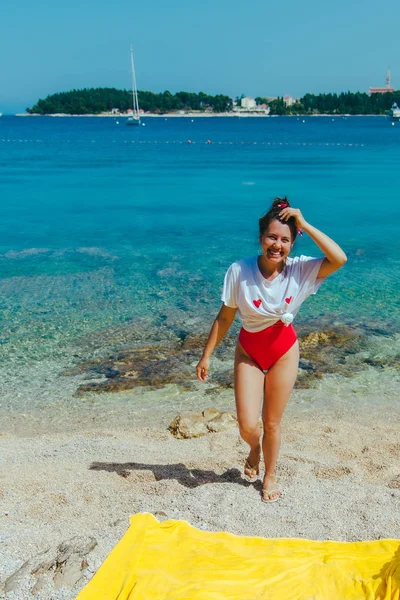 Молодая красивая женщина в красном купальнике и белой футболке на морском пляже — стоковое фото