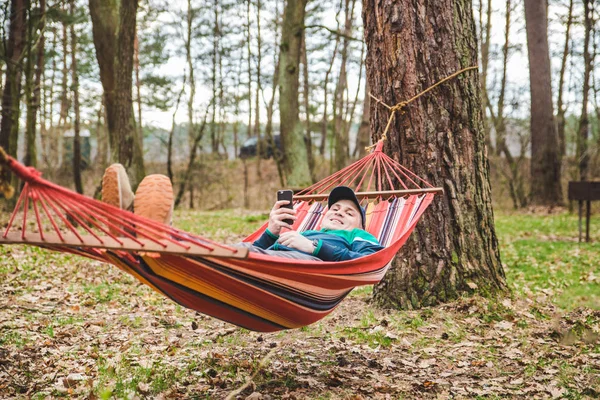 Young man laying in hammock surfing in phone — Stock Photo, Image