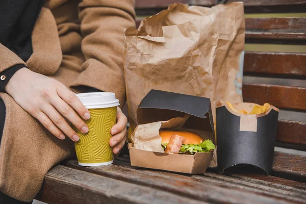 Las manos de mujer cierran sosteniendo hamburguesa con taza de café. comida rápida — Foto de Stock