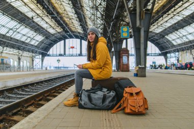 genç kadın çantalarında tren istasyonunda oturup. Treni bekliyorum. kopyalama alanı