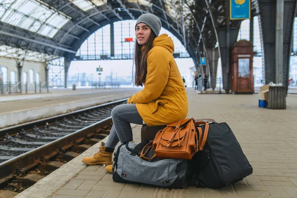 Молодая женщина сидит на железнодорожной станции на своих сумках. Жду поезда. копировальное пространство — стоковое фото