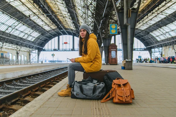 Молодая женщина сидит на железнодорожной станции на своих сумках. Жду поезда. копировальное пространство — стоковое фото
