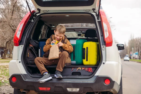 Little kid looking into paper bag with candies sitting in car trunk — Stock Photo, Image