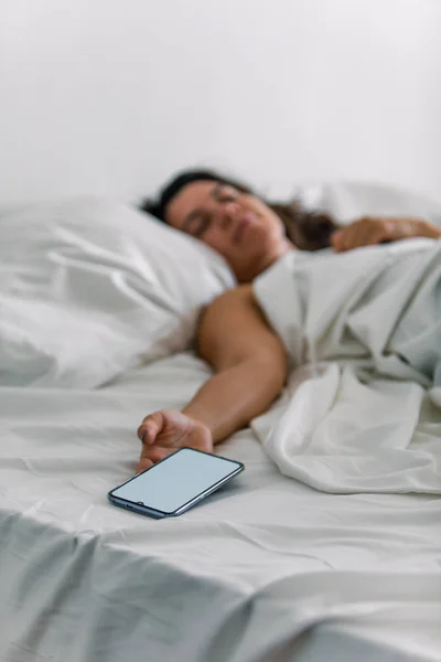 Жінка спить в ліжку телефон в руці — стокове фото