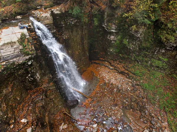 Человек, стоящий на скале и смотрящий на водопад осенним временем — стоковое фото