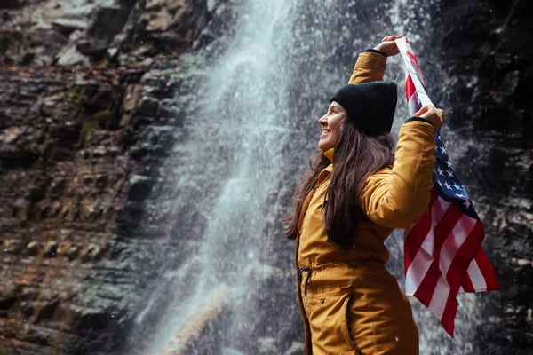 Young caucasian adult female with usa flag in front of waterfall — Stock Photo, Image